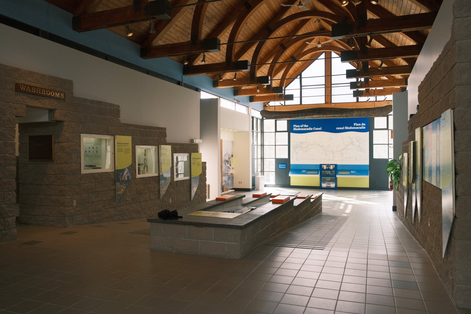 The main hall of the Fairbanks Interpretive Centre — a working lock model down the centre of the room, wall panels along the sides, and the canal plan wall with its touchscreens at the far end