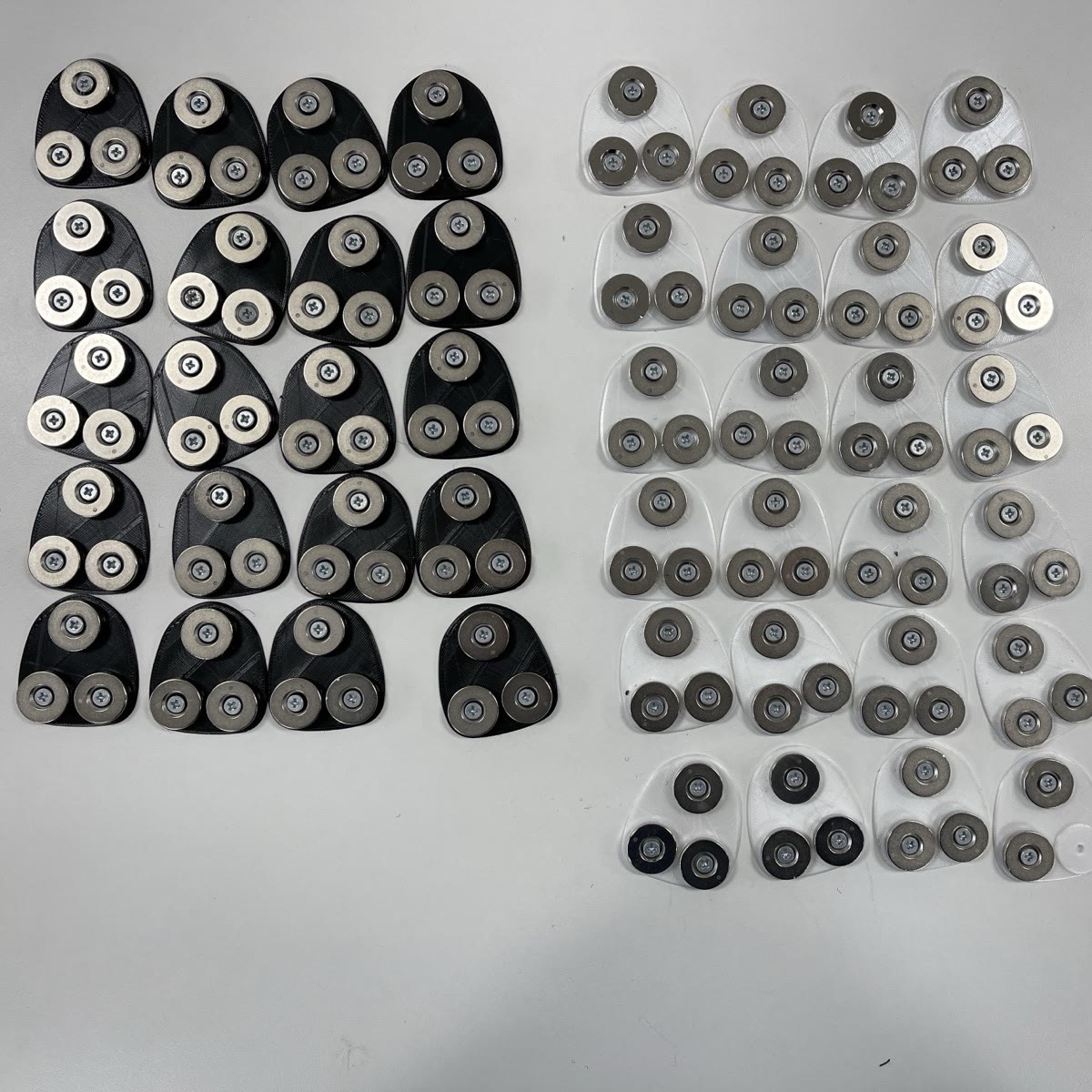 Around forty assembled magnet mounts laid out in two batches, black and clear, for a production run